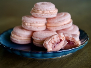 strawberry macarons A stack of delicate pink strawberry macarons with creamy filling on a dark blue plate, one broken to show the fruit center.